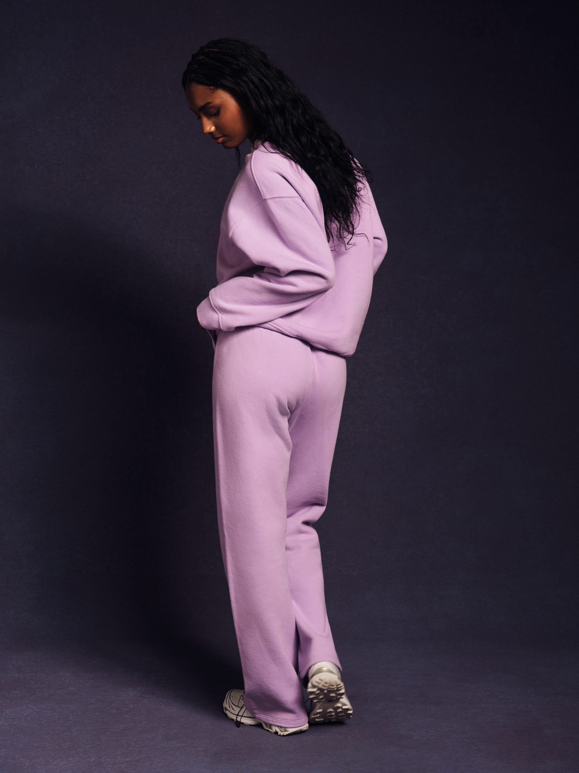 Side profile of a person wearing a light purple tracksuit against a dark background