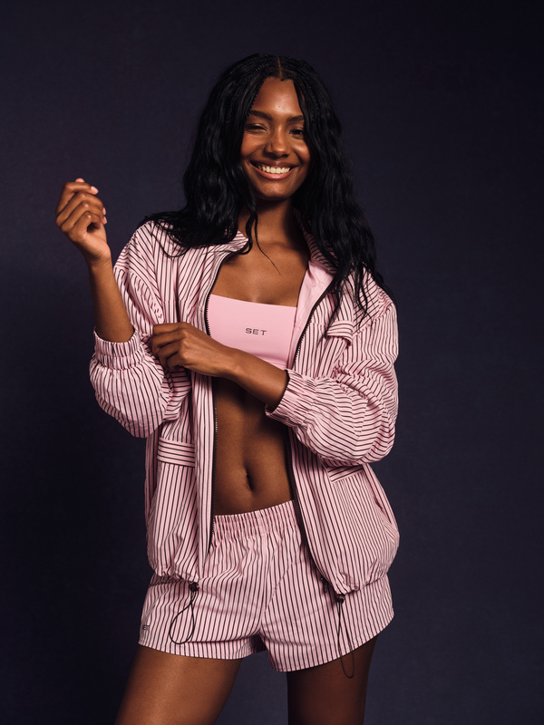 Woman wearing a pink striped shirt and shorts set against a dark background 