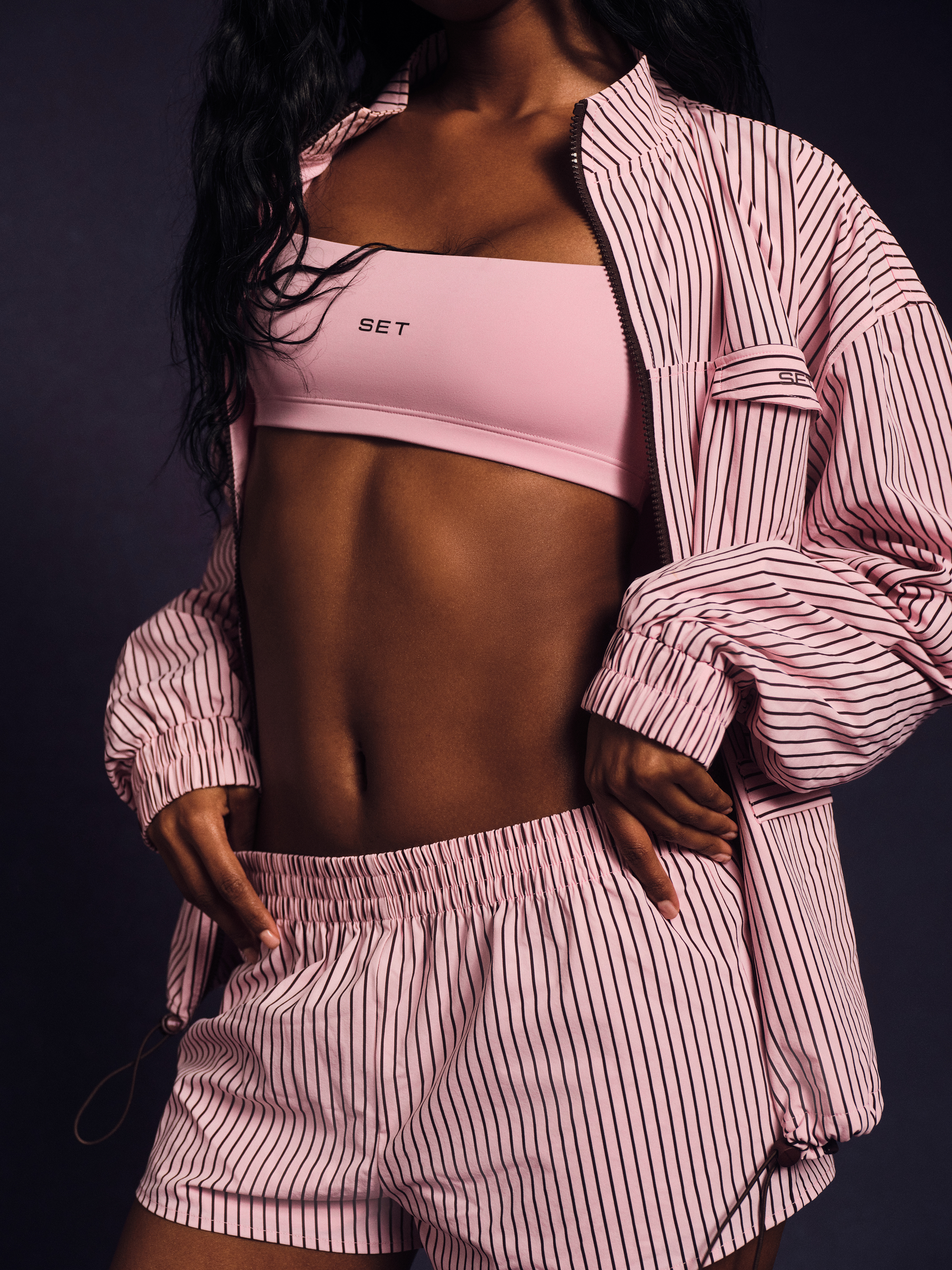 Person wearing a pink sports bra and shorts with a matching striped shirt against a dark background