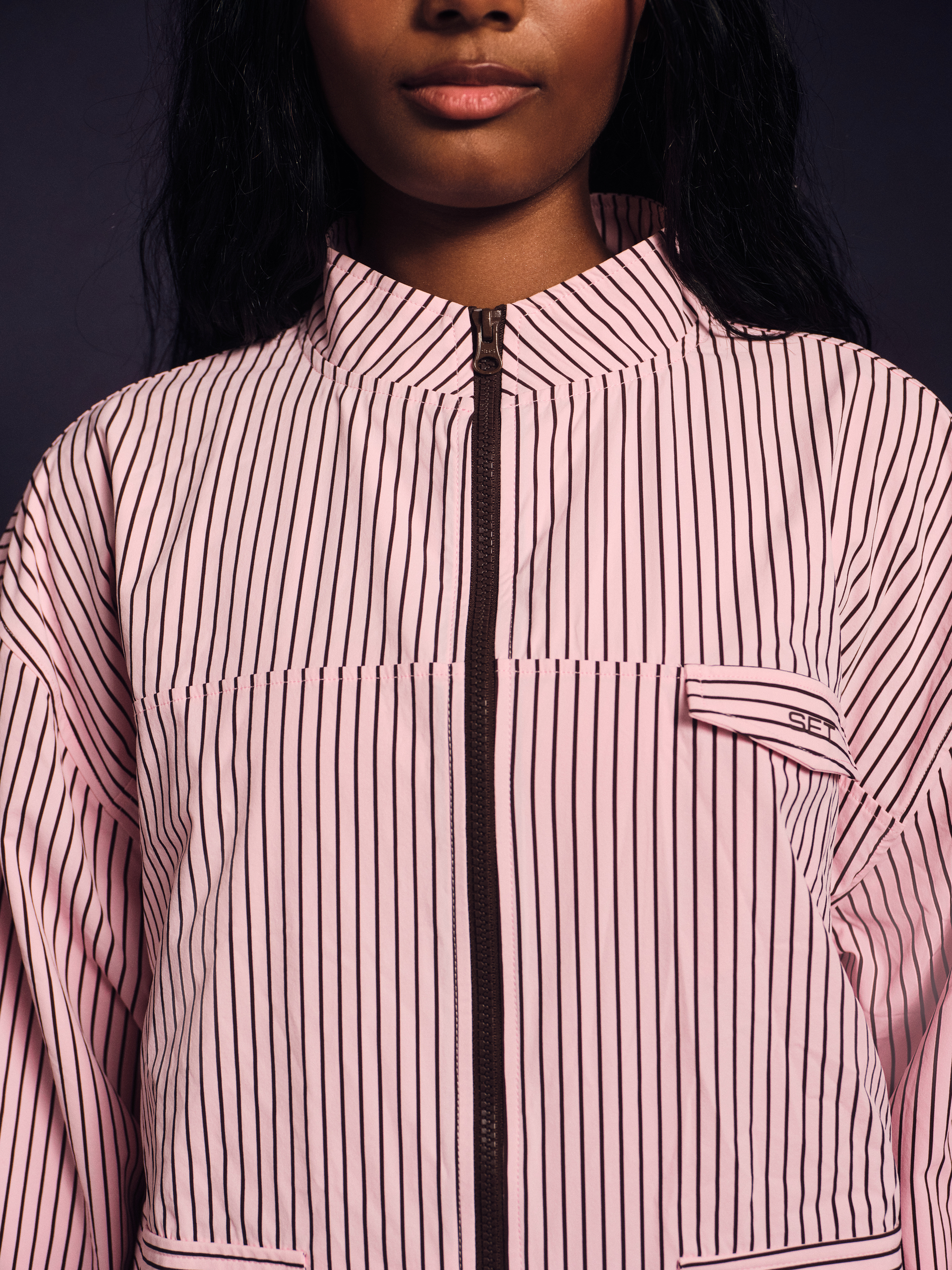 Person wearing a pink and white striped jacket with a dark background