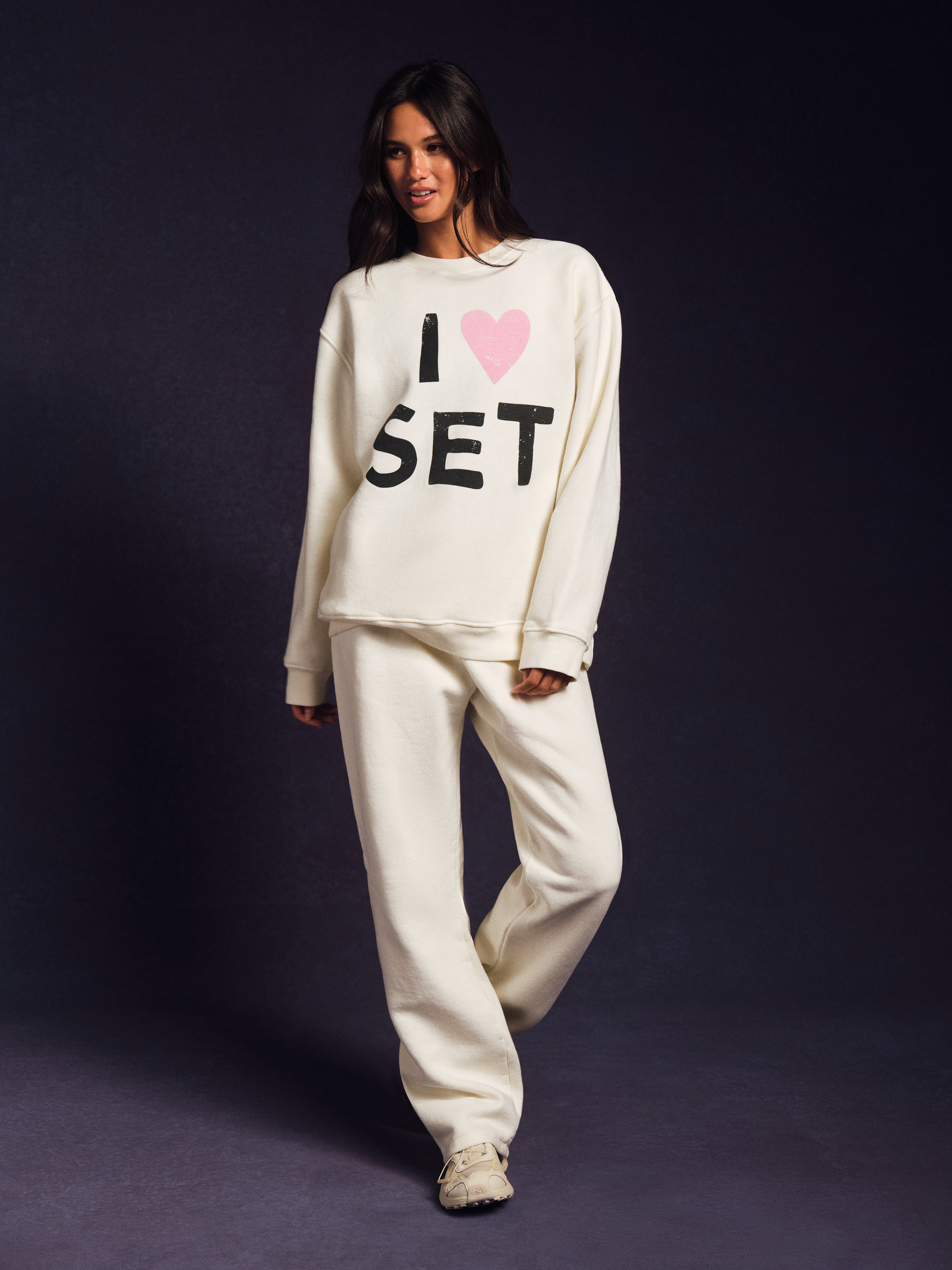 Woman wearing a white sweatshirt with 'I ❤️ SET' text on a dark background <model-info>Jelene wears a size S and is 5’7”, 23” waist, 32AB bust.</model-info>