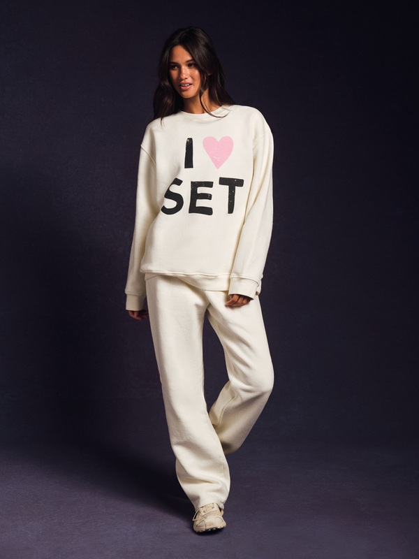 Woman wearing a white sweatshirt with 'I ❤️ SET' text on a dark background 