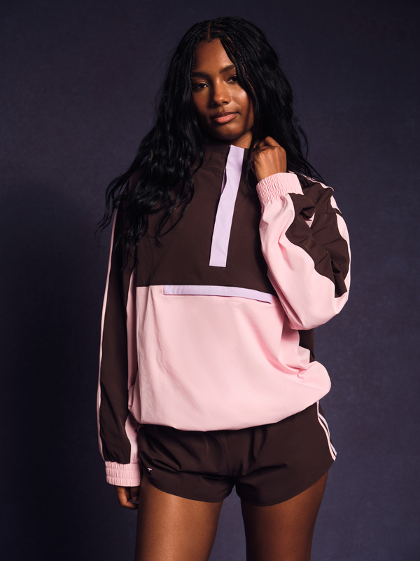 Person wearing a brown and pink tracksuit against a dark background 