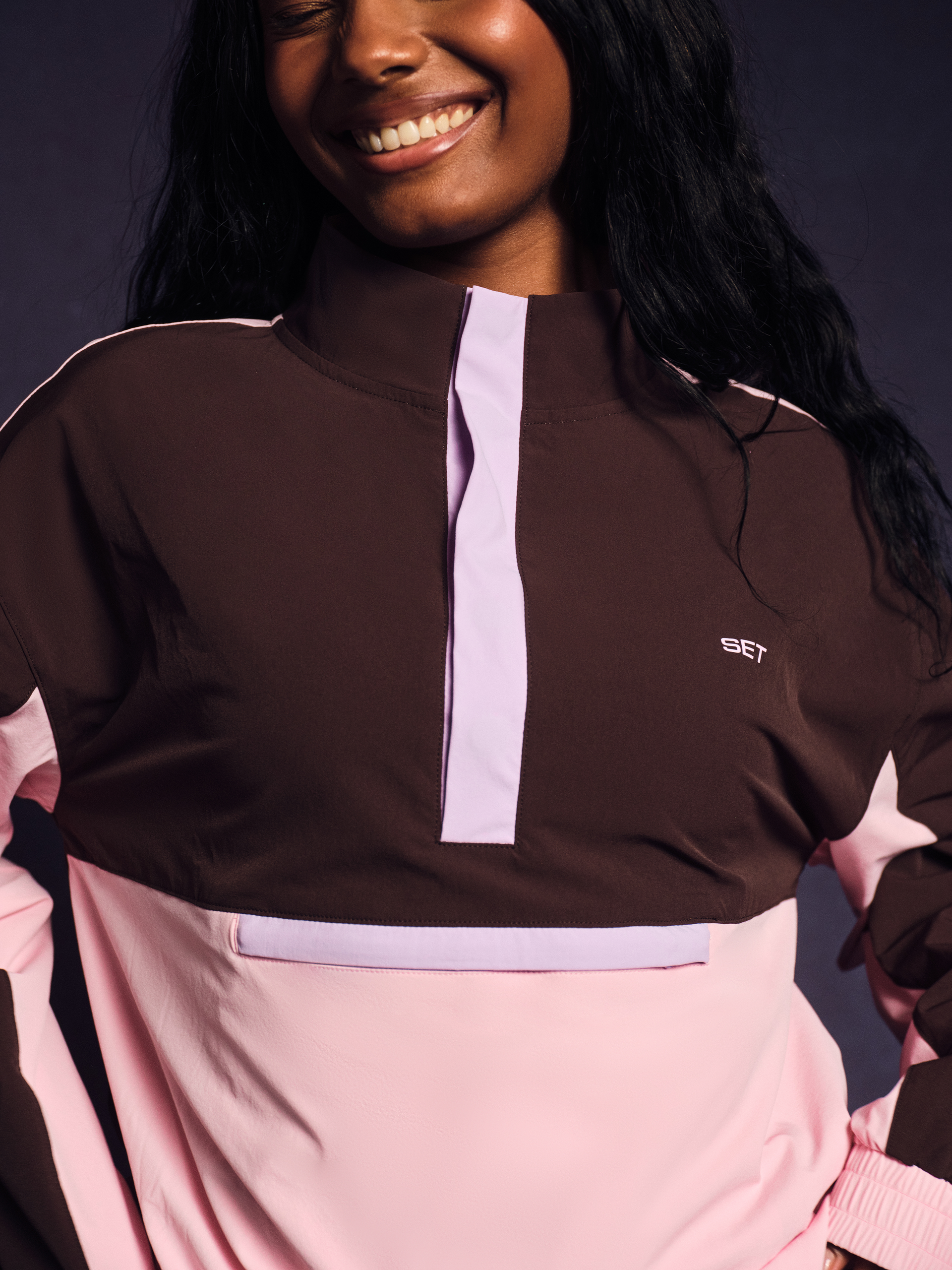 Person wearing a brown and pink outfit with a visible brand logo on a dark background