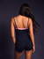 Person wearing a black bodysuit with pink straps against a dark background