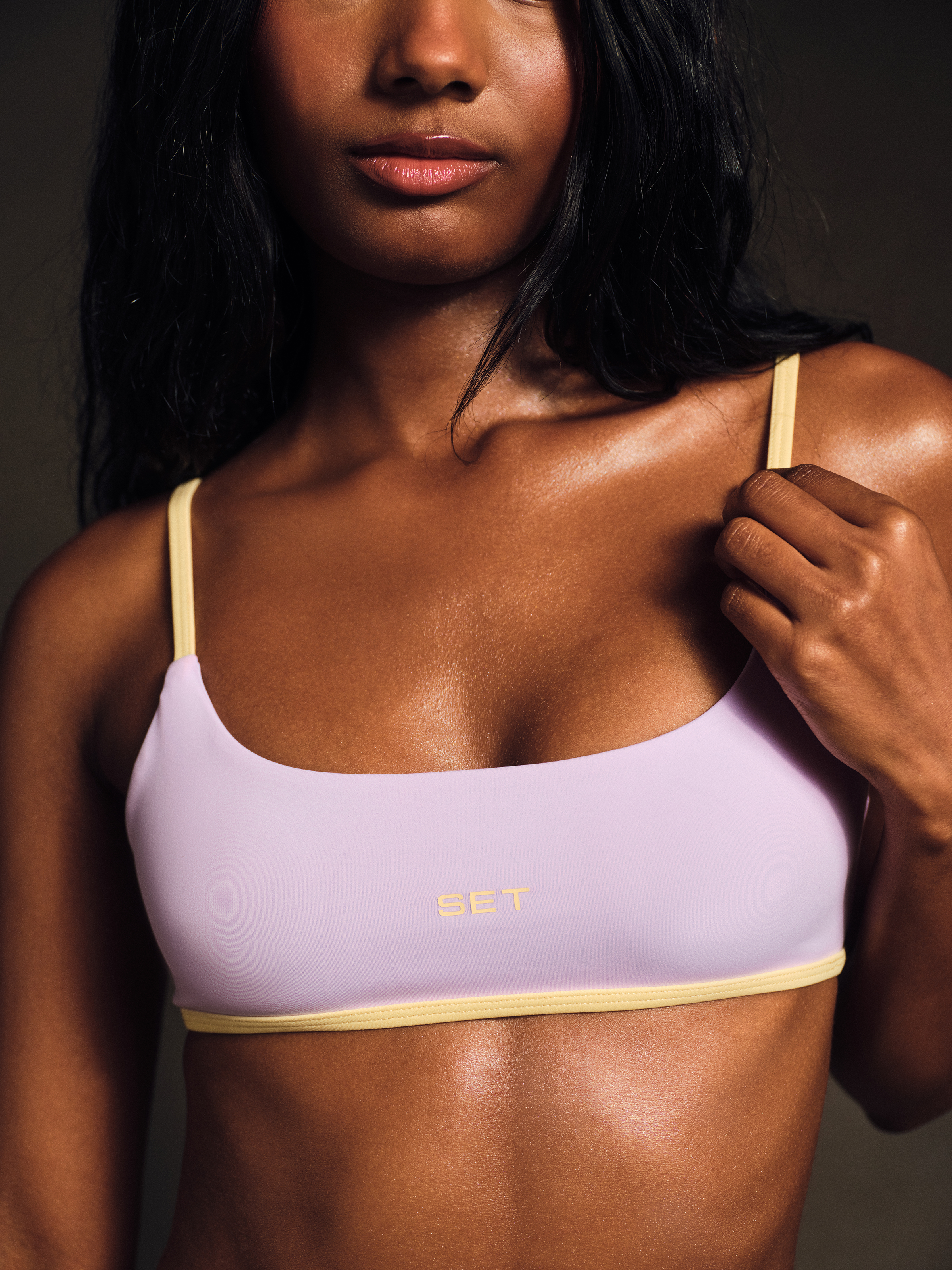 Woman wearing a purple sports bra and yellow shorts against a dark background. 