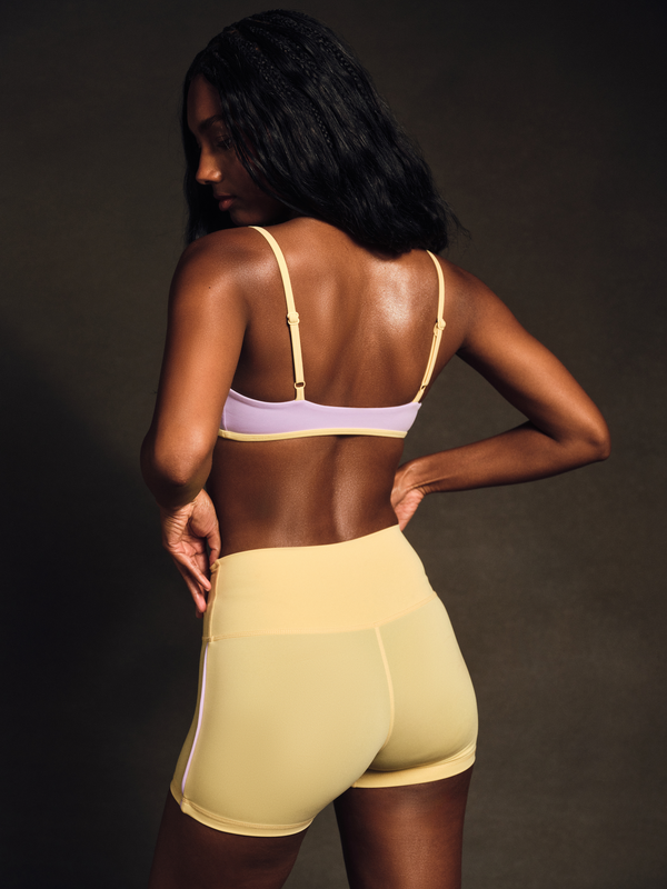Woman wearing a yellow sports bra and shorts on a dark background
