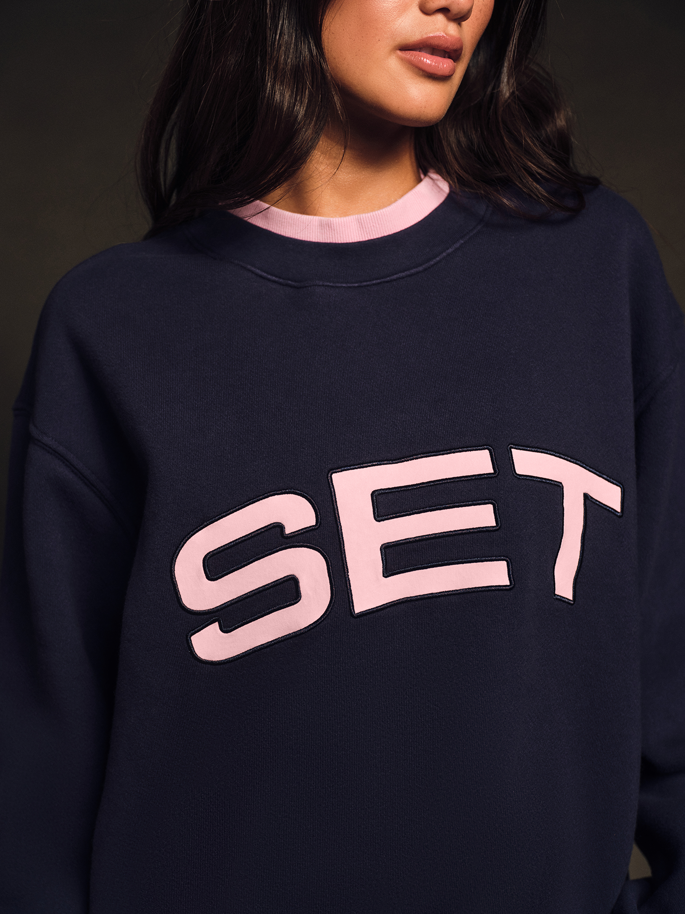Person wearing a navy sweatshirt with 'SET' in pink text on a dark background