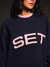 Person wearing a navy sweatshirt with 'SET' in pink text on a dark background