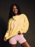 Woman wearing a yellow sweatshirt with 'SET' in pink letters and pink shorts on a dark background <model-info>Umi wears a size S and is 5’8½”, 23½” waist, 32B bust.</model-info>