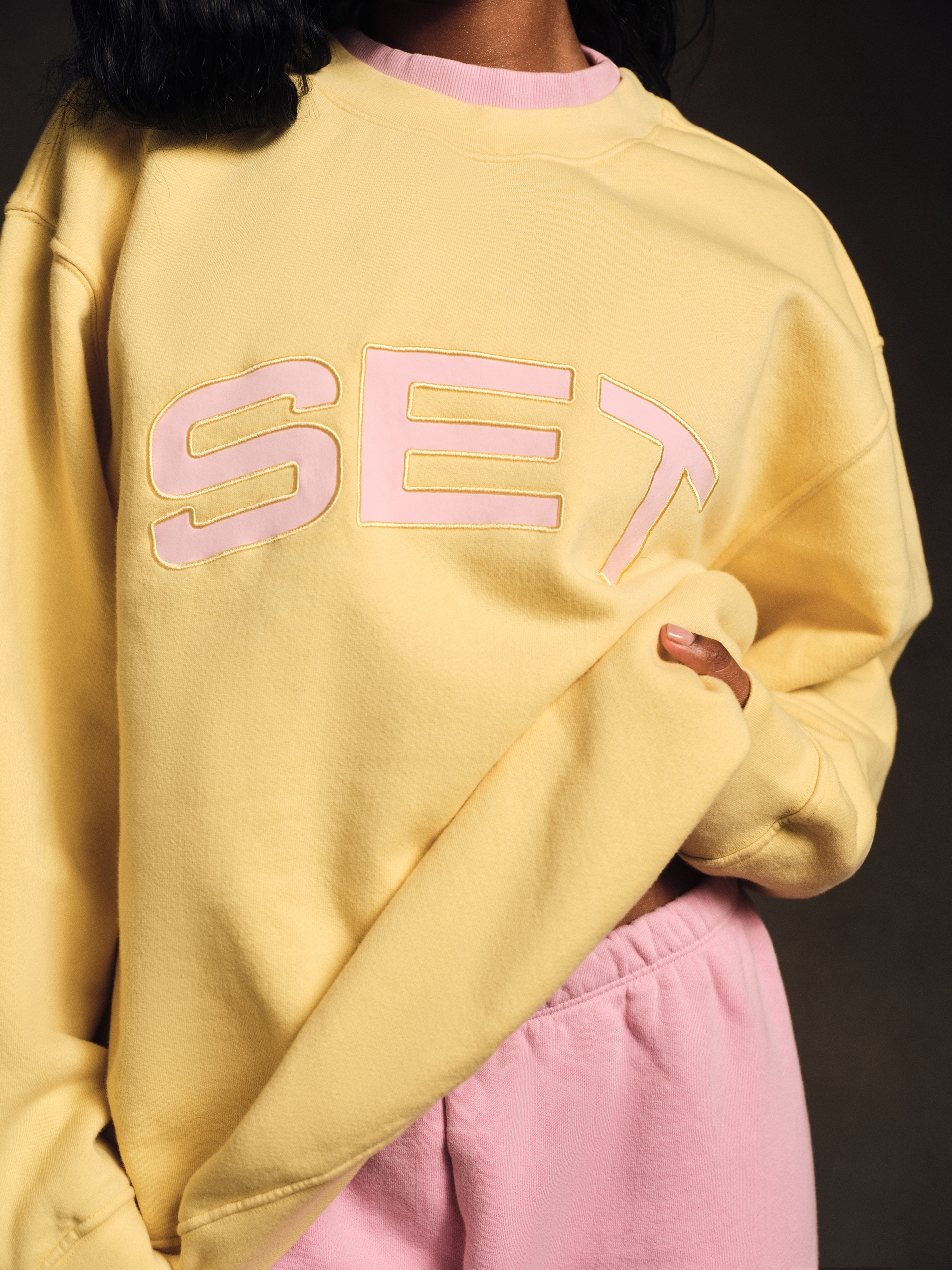 Person wearing a yellow sweatshirt with 'SET' printed in pink on a dark background