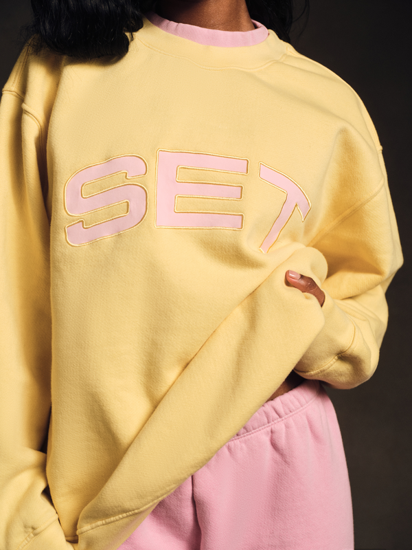 Person wearing a yellow sweatshirt with 'SET' printed in pink on a dark background
