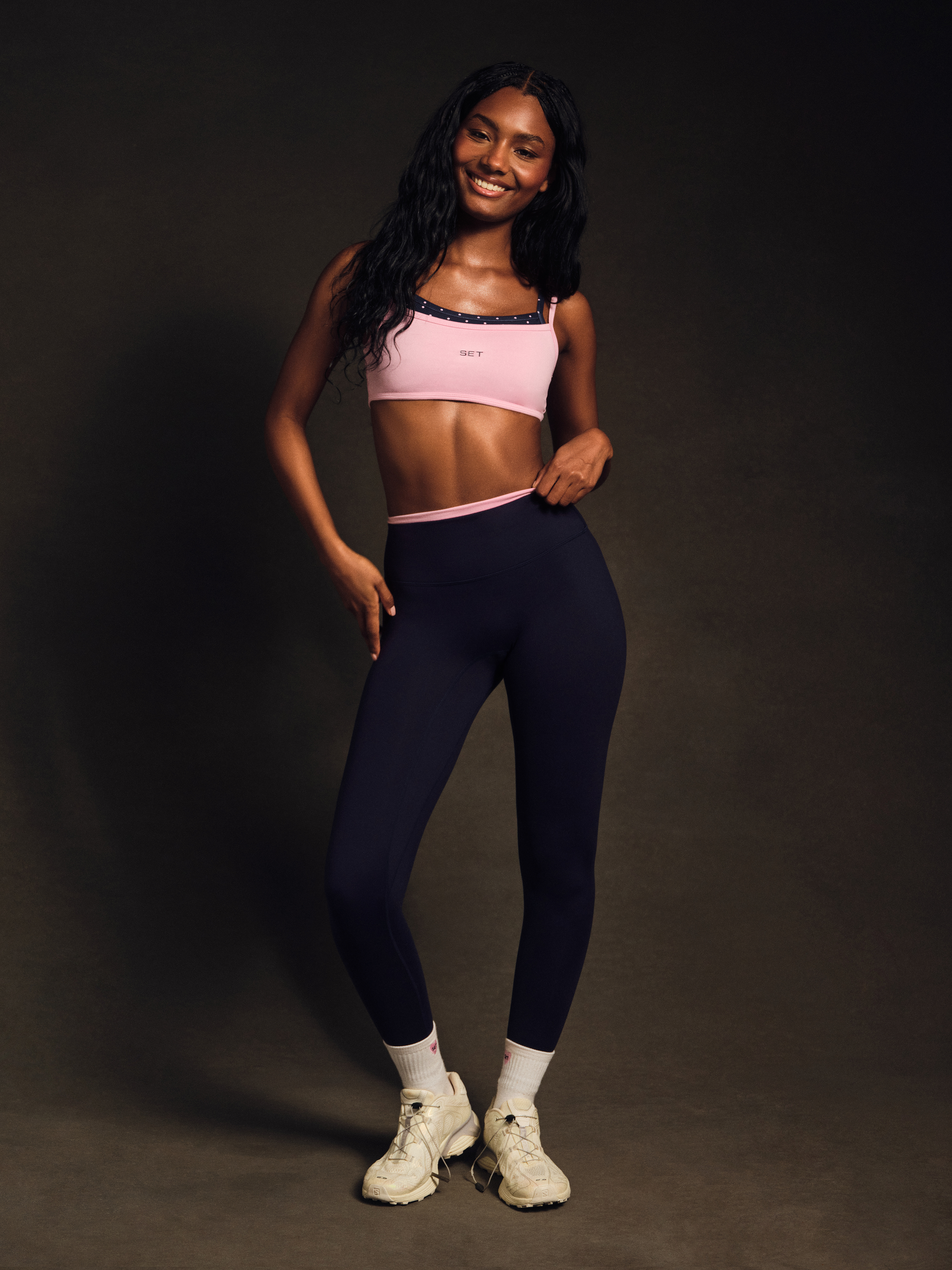 Woman wearing a pink sports bra and dark blue leggings on a dark background 