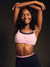 Woman wearing a pink sports bra and black leggings with a dark background  <model-info>Umi wears a size XS and is 5’8½”, 23½” waist, 32B bust.</model-info>