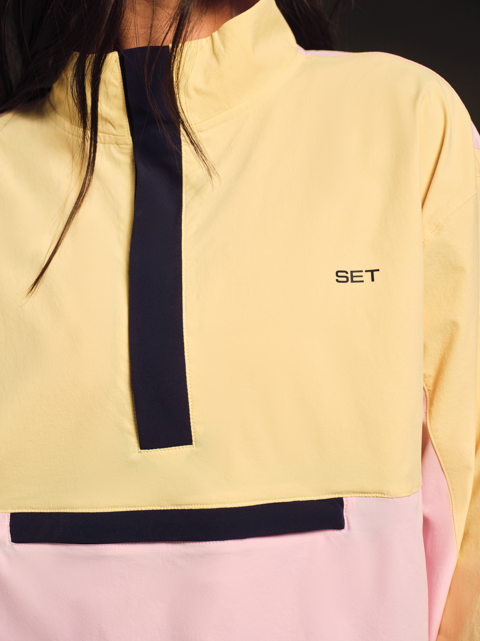Close-up of a person wearing a yellow and pink jacket with a black stripe and 'SET' logo.