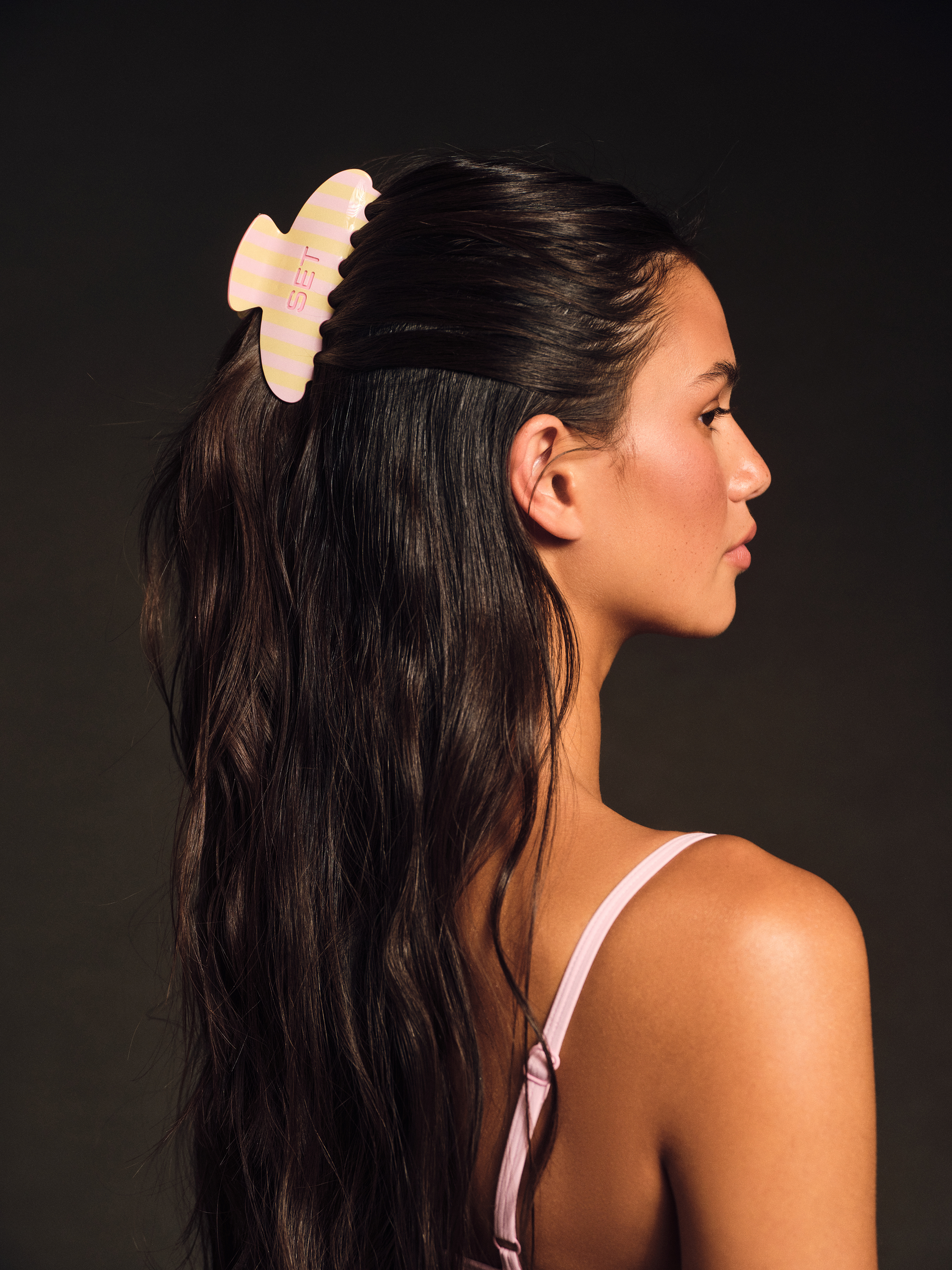Woman with a yellow hair accessory in her dark hair against a dark background