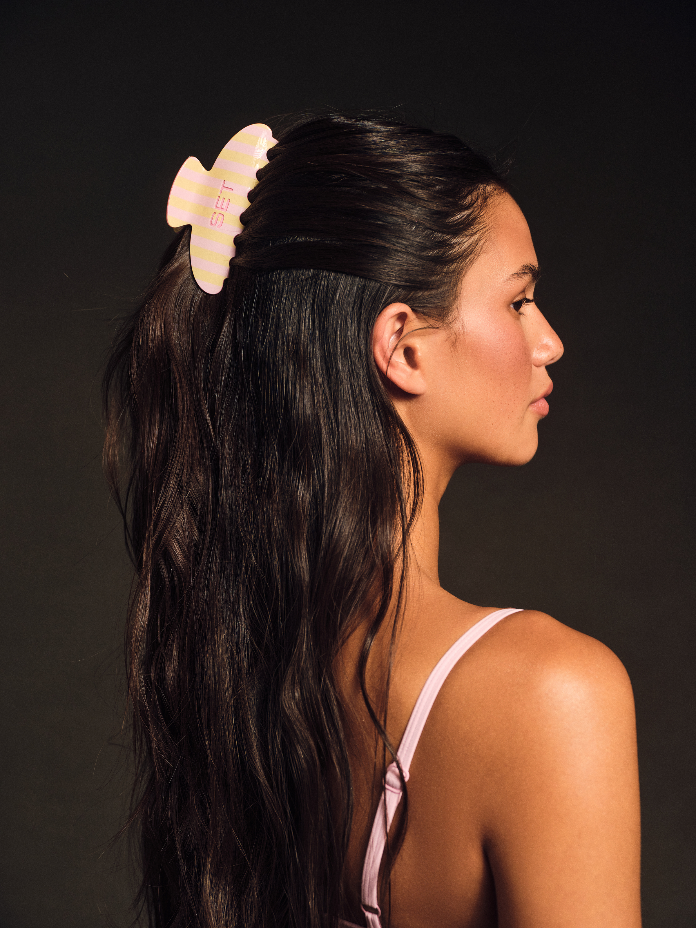 Woman with a yellow hair accessory in her dark hair against a dark background