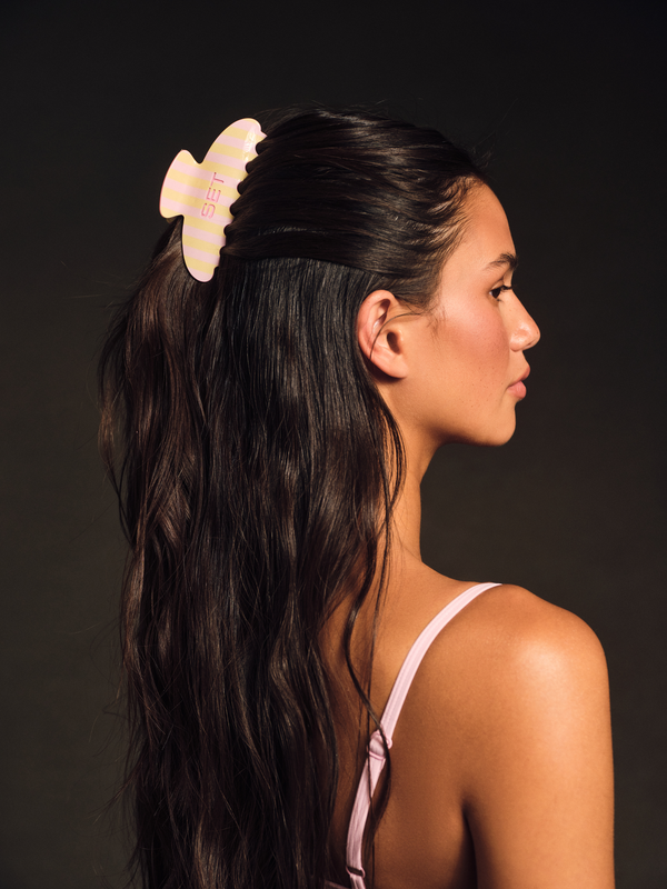 Woman with a yellow hair accessory in her dark hair against a dark background