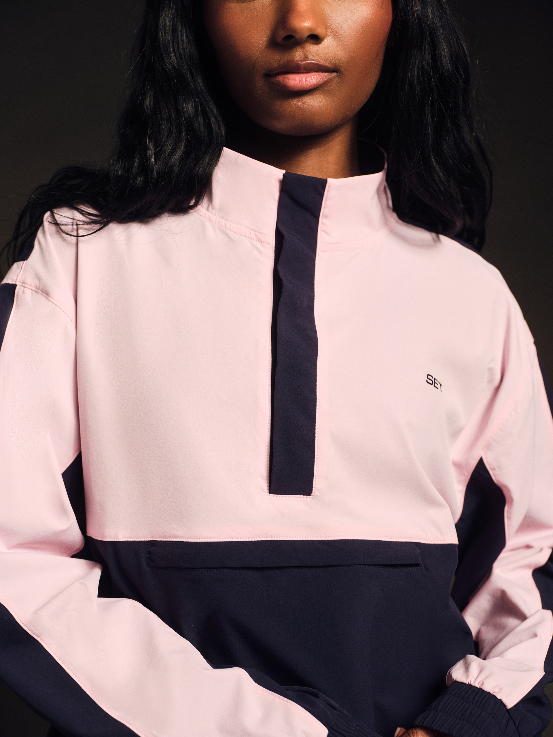 Person wearing a pink and navy outfit with a brand logo on a dark background