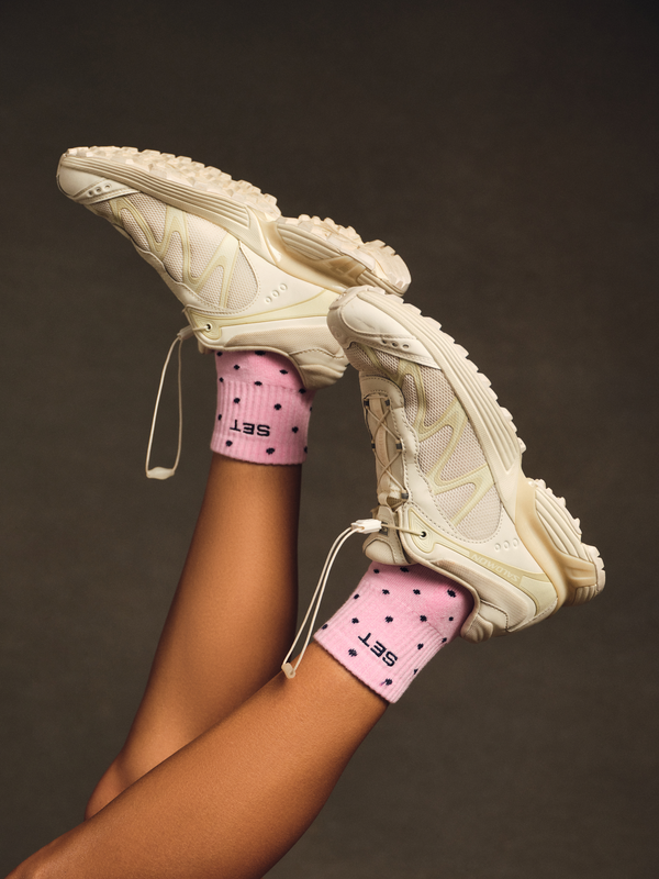 Person wearing white shoes with pink socks and navy polka dots.