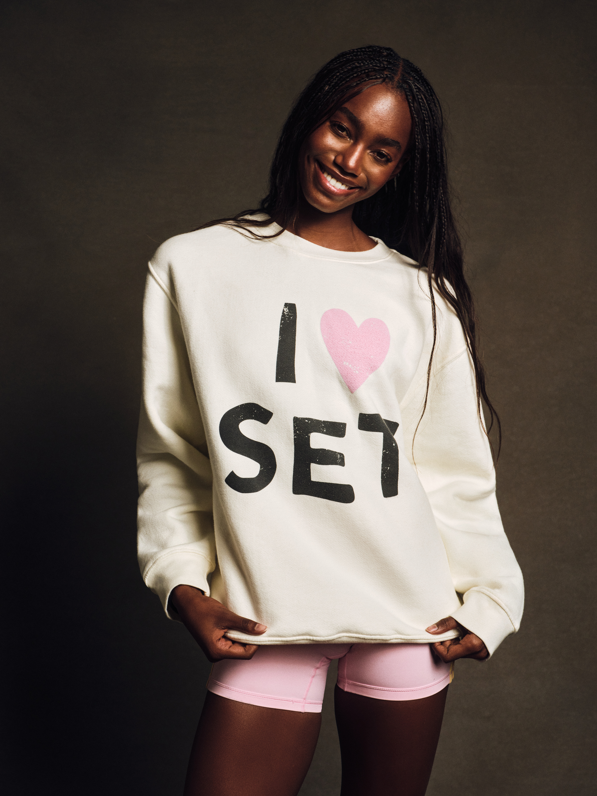 Woman wearing a white sweatshirt with 'I ❤️ SET' text on a dark background <model-info>Nina D wears a size XS/S and is 5’10”, 24” waist, 31½" bust.</model-info>