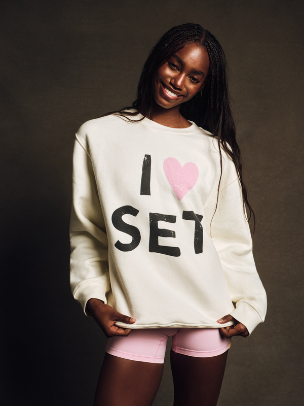Woman wearing a white sweatshirt with 'I ❤️ SET' text on a dark background 