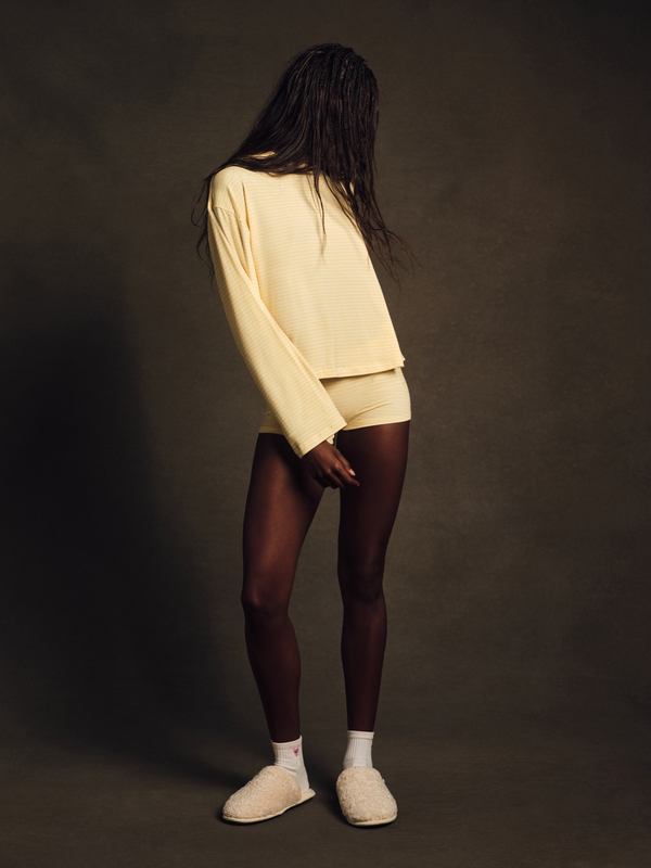 Person wearing a light-colored sweater and dark leggings against a brown background