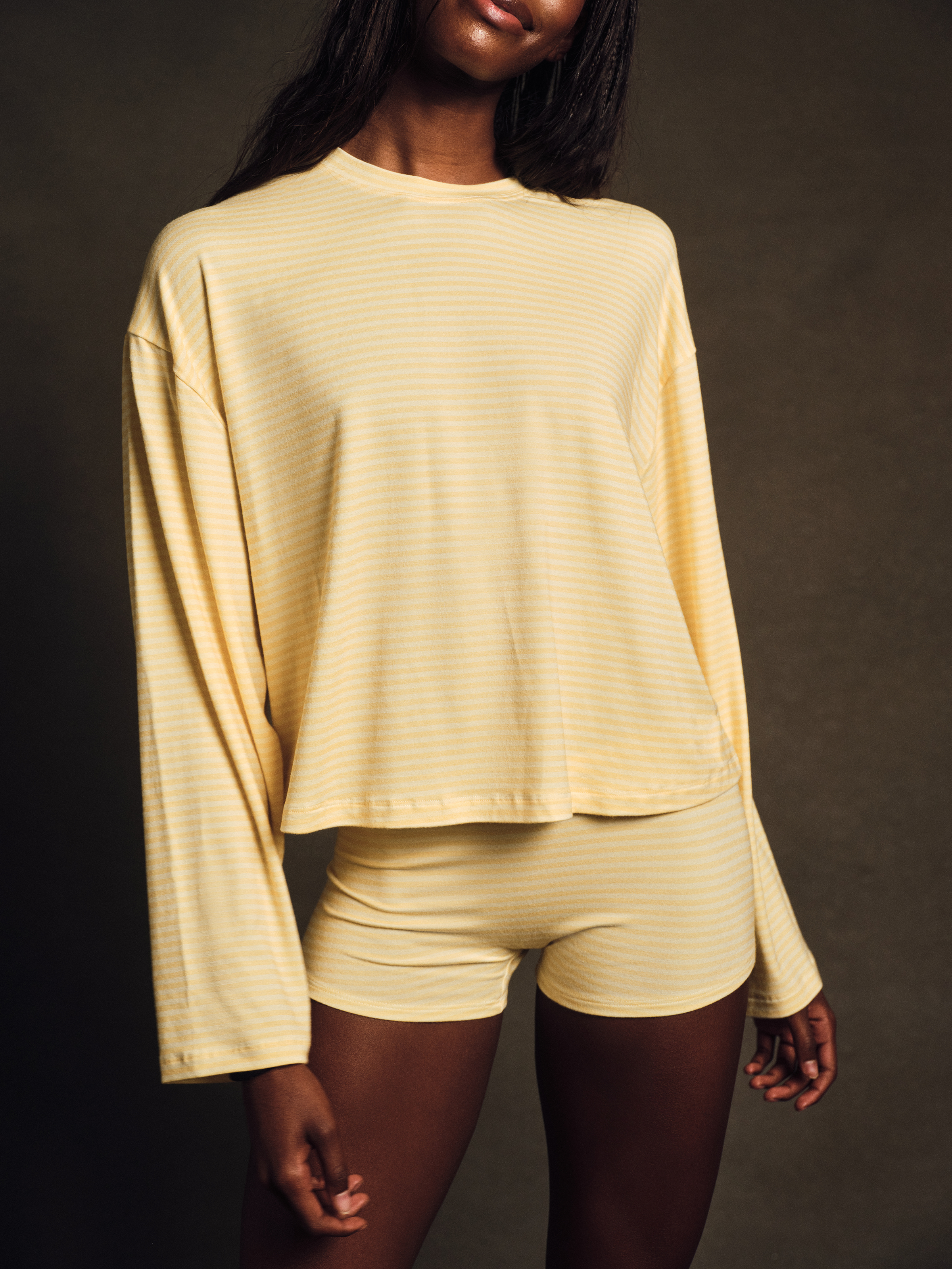 Woman wearing a yellow long-sleeve top and shorts against a dark background