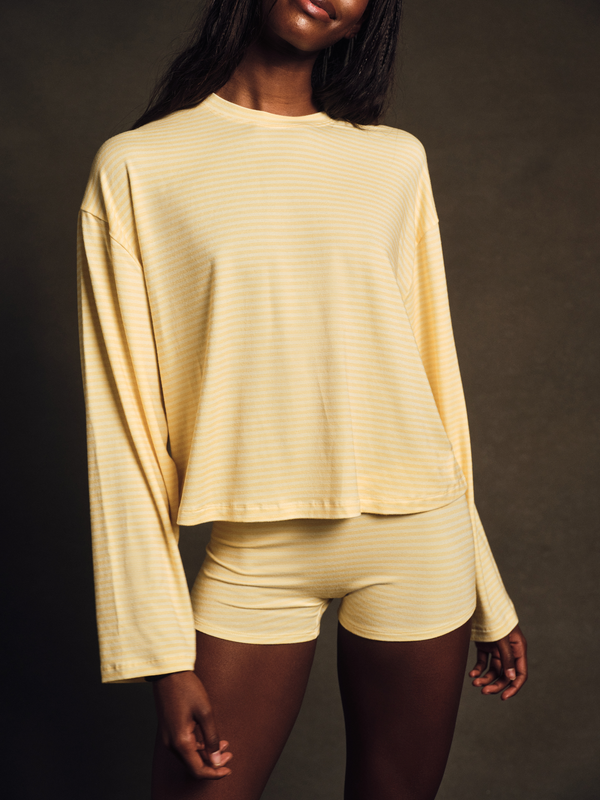 Woman wearing a yellow long-sleeve top and shorts against a dark background