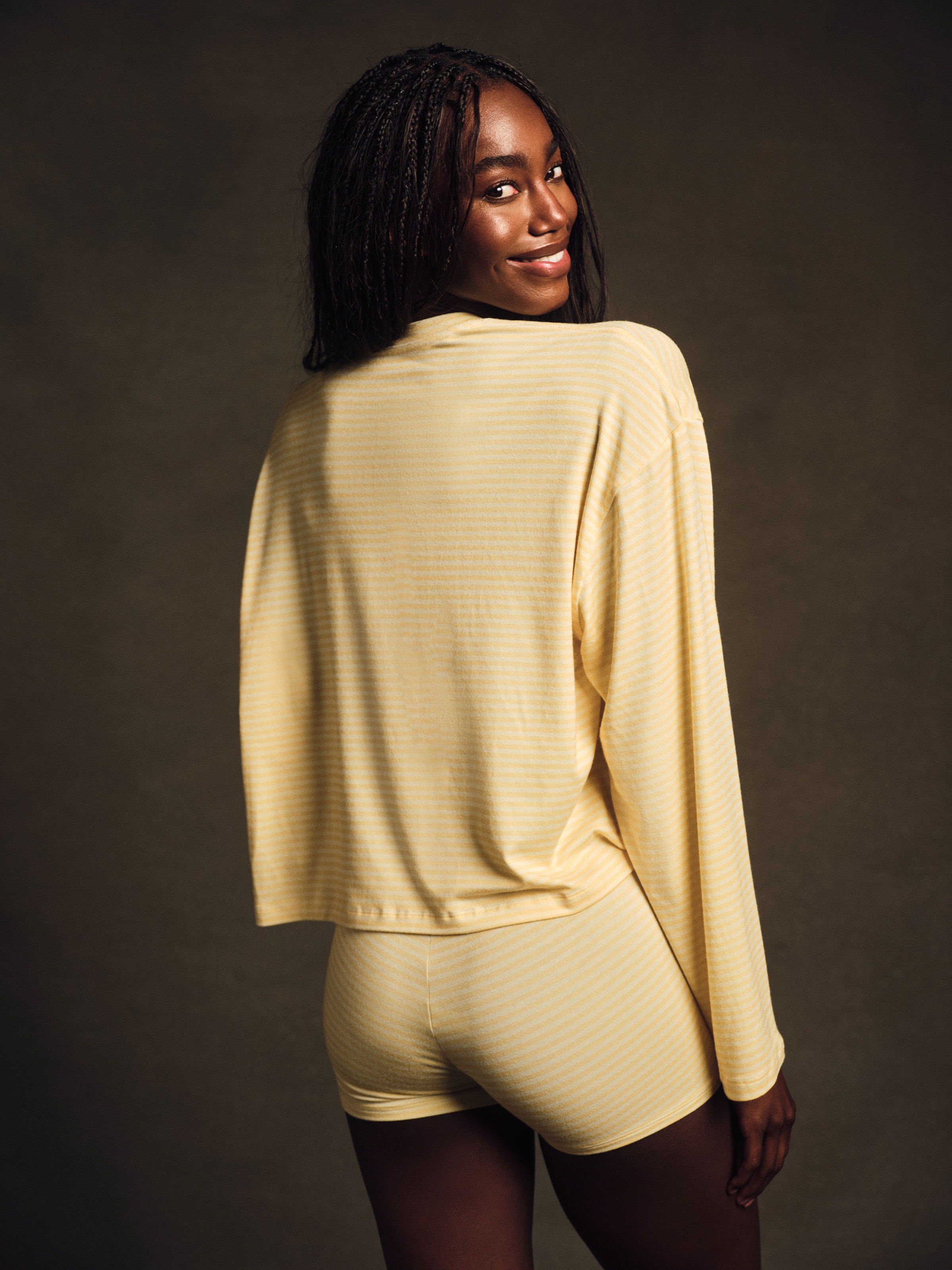 Woman wearing a beige long-sleeve top and shorts against a dark background 