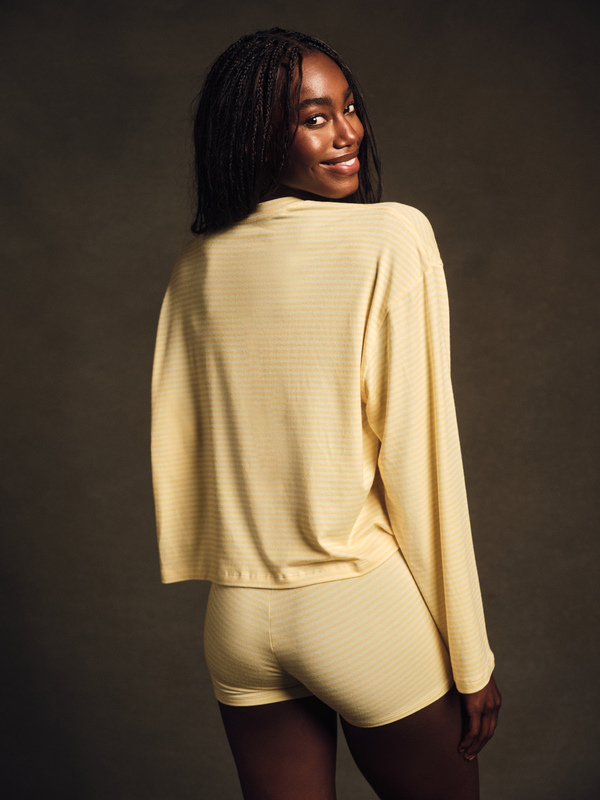 Woman wearing a beige long-sleeve top and shorts against a dark background 