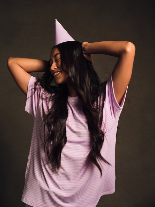 Woman wearing a purple dress and party hat against a dark background