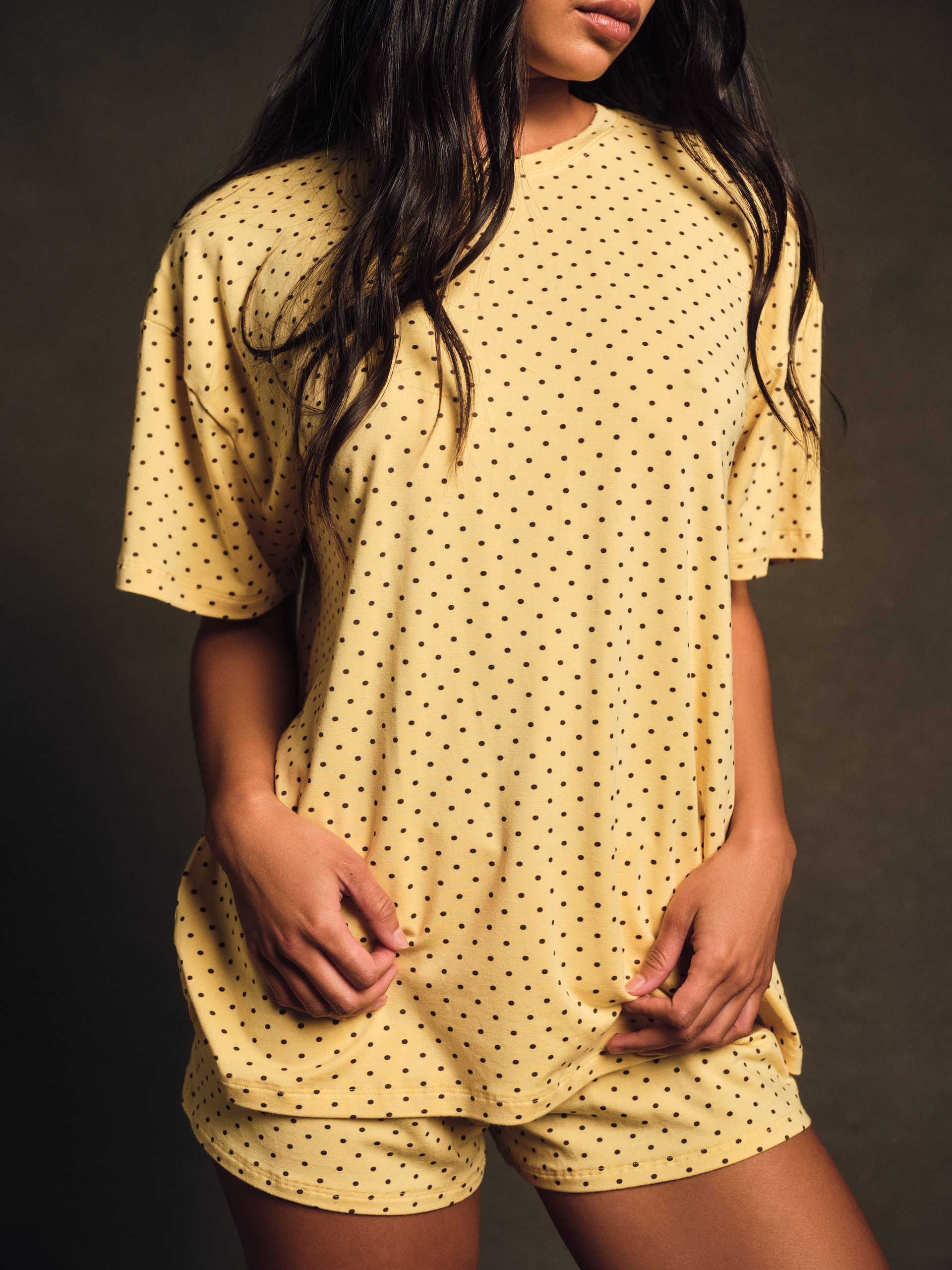 Woman wearing a yellow polka dot outfit against a dark background <model-info>Amber wears a size S and is 5’½”, 22½” waist, 30B" bust.</model-info>