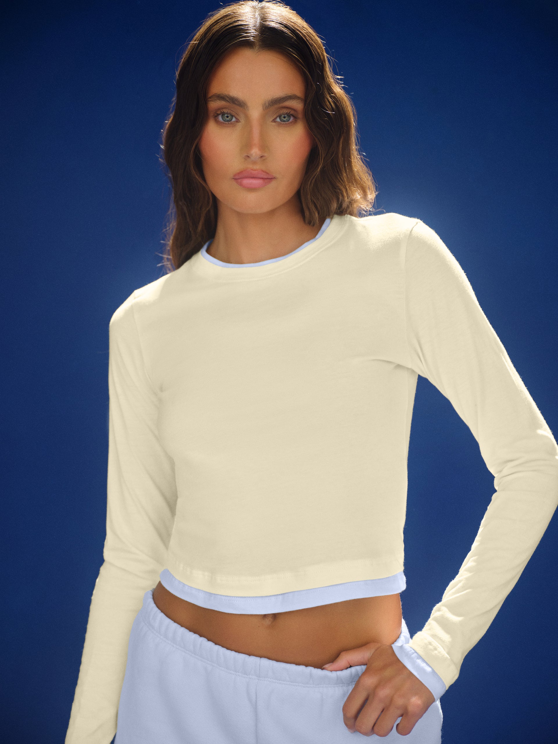 Woman wearing a light-colored long-sleeve top against a blue background <model-info>Logan wears a size S and is 5’9½”, 24” waist, 32B bust.</model-info>