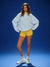 Woman wearing a light blue sweatshirt, yellow shorts, and white sneakers on a blue background