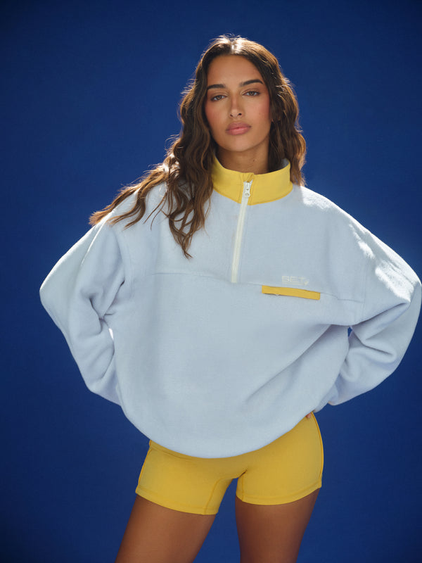 Woman wearing a light blue pullover with yellow accents against a blue background 