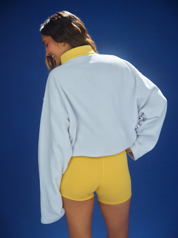 Person wearing a light blue sweatshirt and yellow shorts against a blue background 