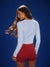 Woman wearing a white long-sleeve top and red shorts against a blue background