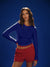 Woman wearing a blue long-sleeve top and red shorts against a dark blue background <model-info>Kushi wears a size S and is 5'8, 24” waist, 32C bust.</model-info>