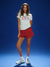 Woman wearing a white t-shirt with red and blue text, red shorts, and white sneakers on a blue background
