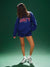 Person wearing a blue sweatshirt and shorts with 'SET' on the back against a green background