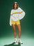 Woman wearing a white sweater with yellow and blue accents and yellow shorts on a green background