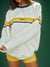 Person wearing a white sweatshirt with yellow and blue stripes on a green background