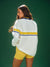 Person wearing a white sweater with yellow stripes and yellow shorts on a green background