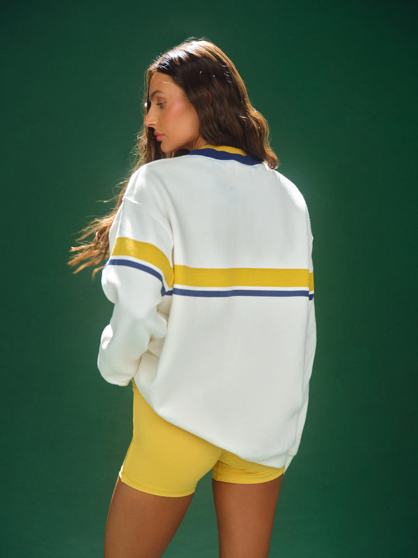 Person wearing a white sweater with yellow stripes and yellow shorts on a green background