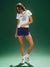 Woman wearing a white t-shirt with a graphic design and blue shorts on a green background
