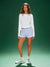 Woman wearing a white long-sleeve top and light purple shorts on a green background 