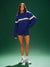 Woman wearing a blue sweater and shorts set with white sneakers on a green background