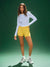 Woman wearing a light blue long-sleeve top and yellow shorts on a green background