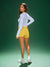 Woman wearing a white long-sleeve top and yellow shorts on a green background